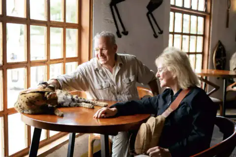 Couple petting a serval cat at lodge table