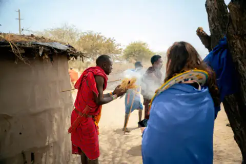 Maasai warrior lighting a fire by friction beside a hut