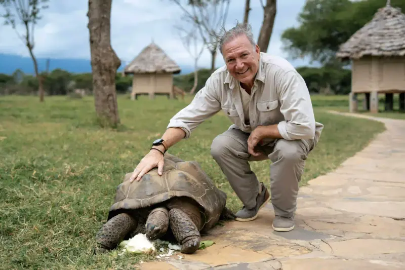 Man crouching beside a giant tortoise
