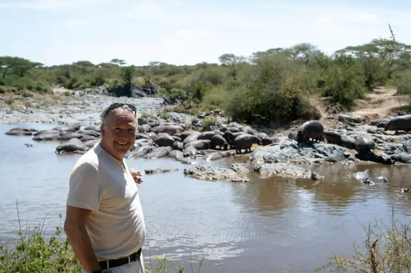 Man standing near a pod of hippos