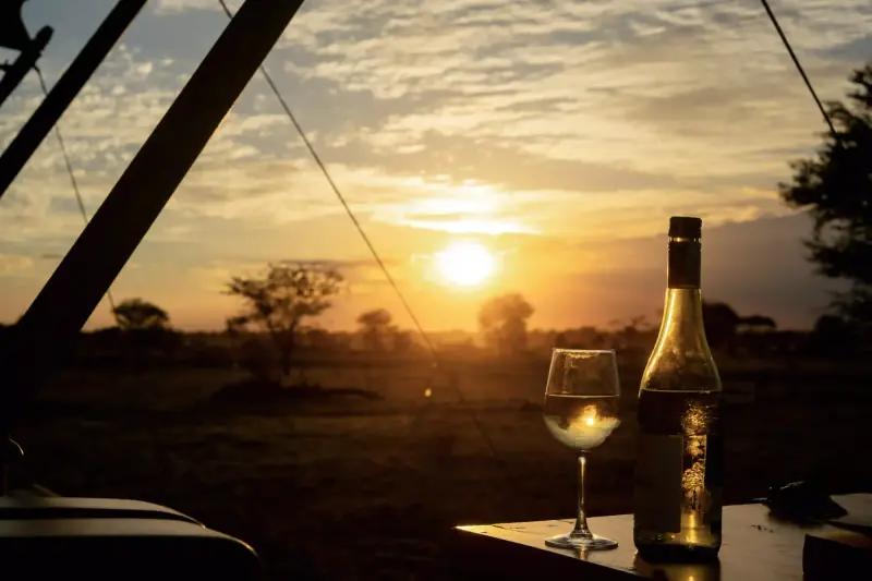 Wine glass and bottle on deck at sunset