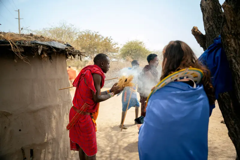 Maasai warrior lighting a fire by friction beside a hut