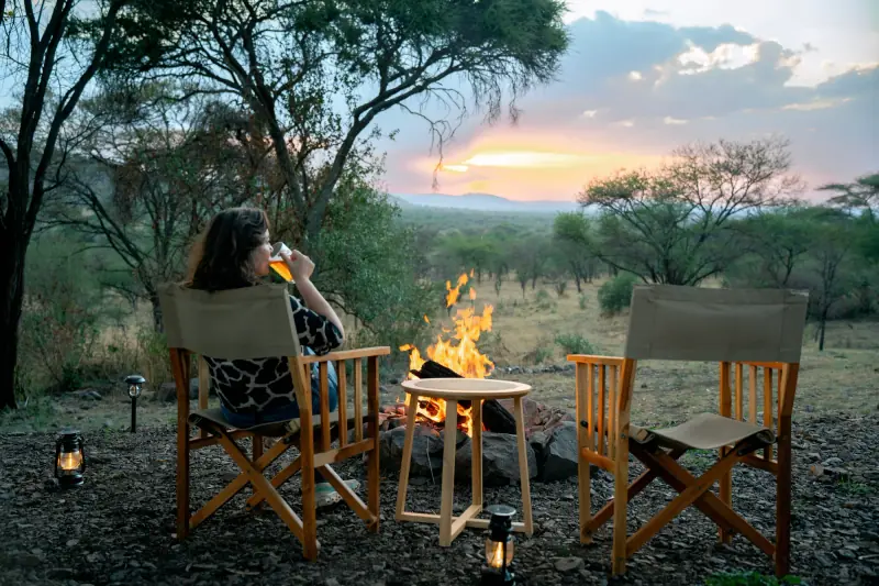 Guest with a drink beside the camp fire pit