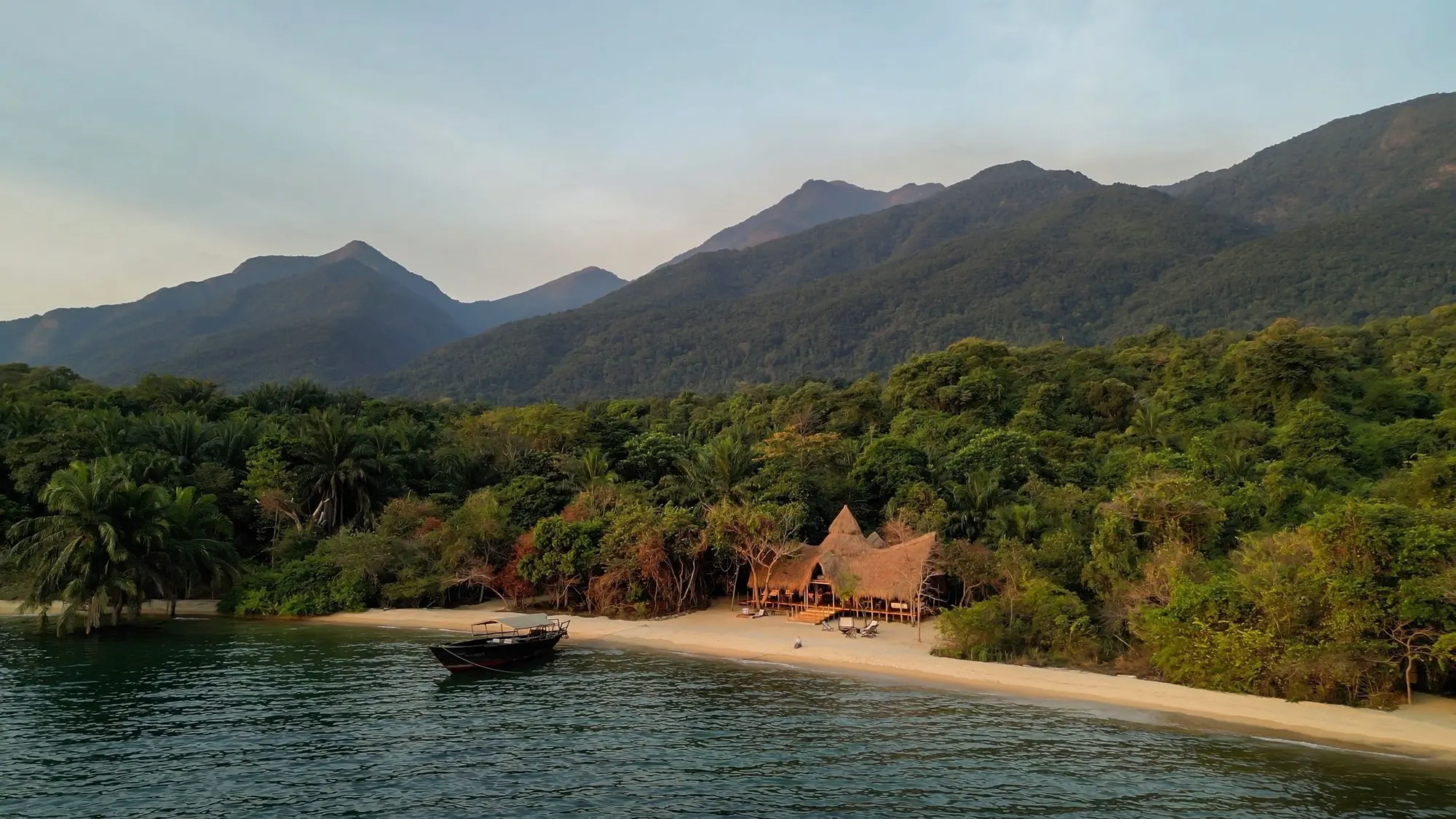 A lodge on a white beach on Lake Tanganyika, the forested Mahale Mountains rising behind